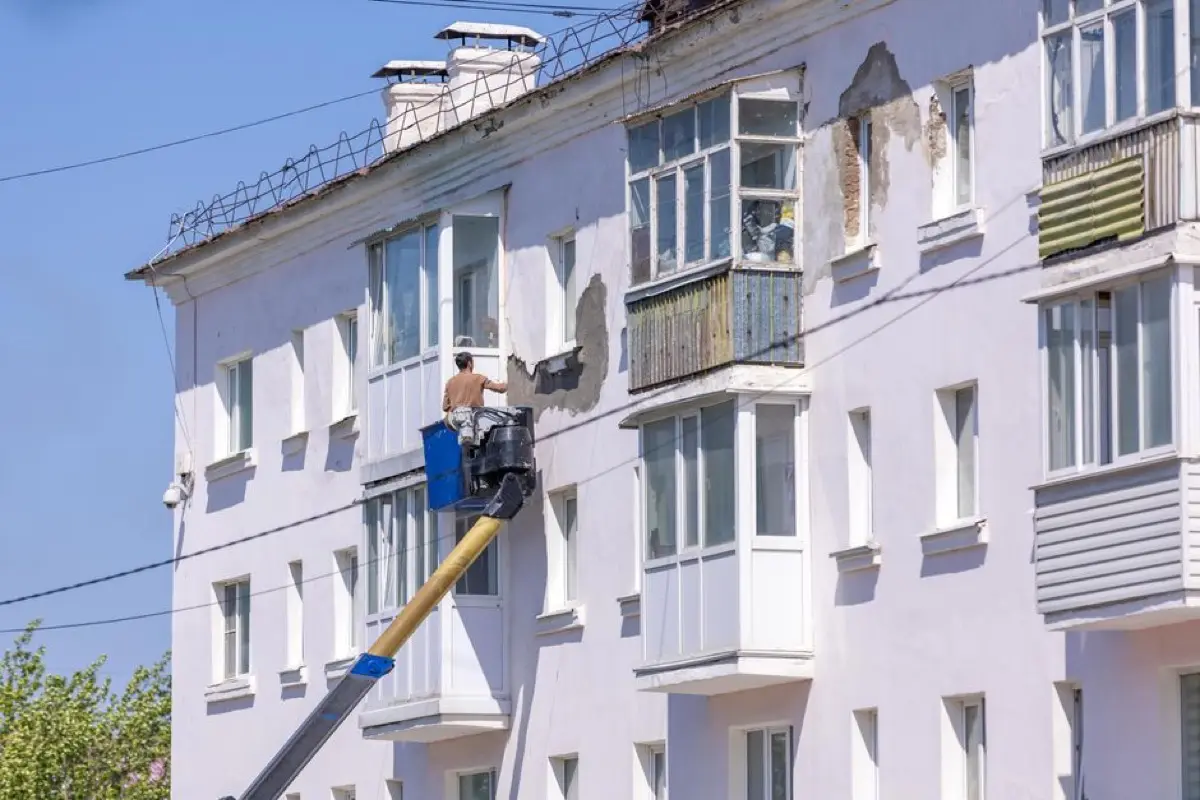Řemeslník na plošině opravuje a zatepluje fasádu bytového domu